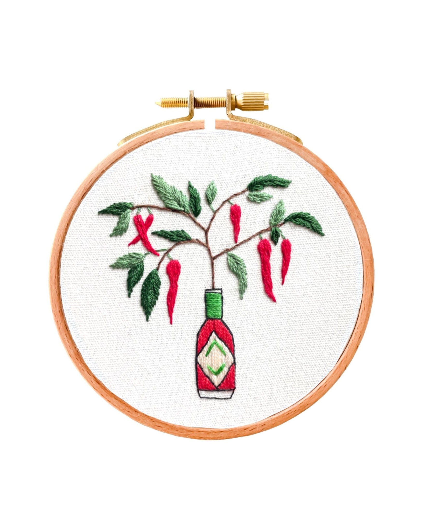 Mini Tabasco Chillies embroidery in wooden hoop showing chillies growing from a Tabasco sauce bottle on white fabric.