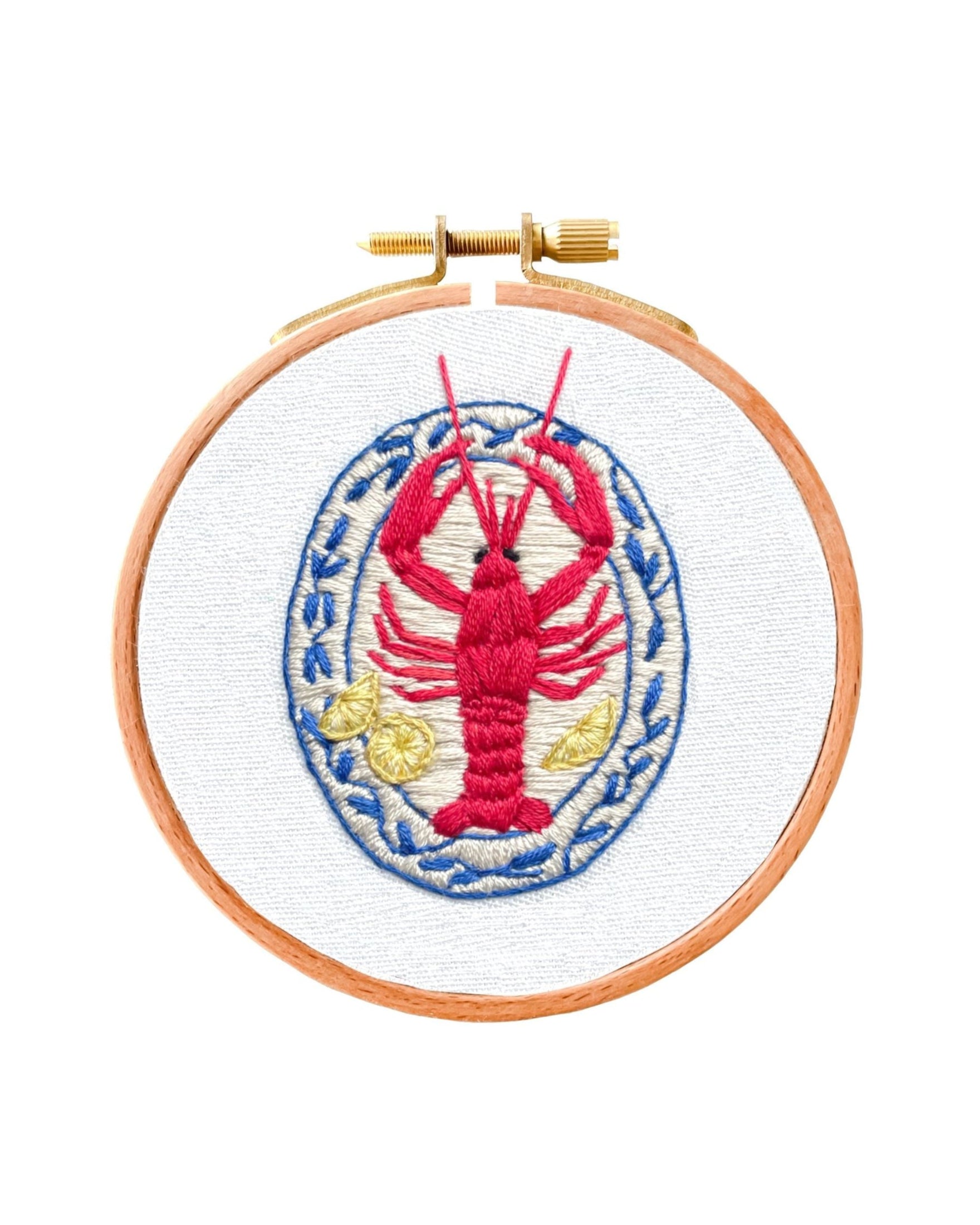 Mini Lobster embroidery design featuring red crustacean with blue oval border and yellow accents on white fabric in wooden hoop