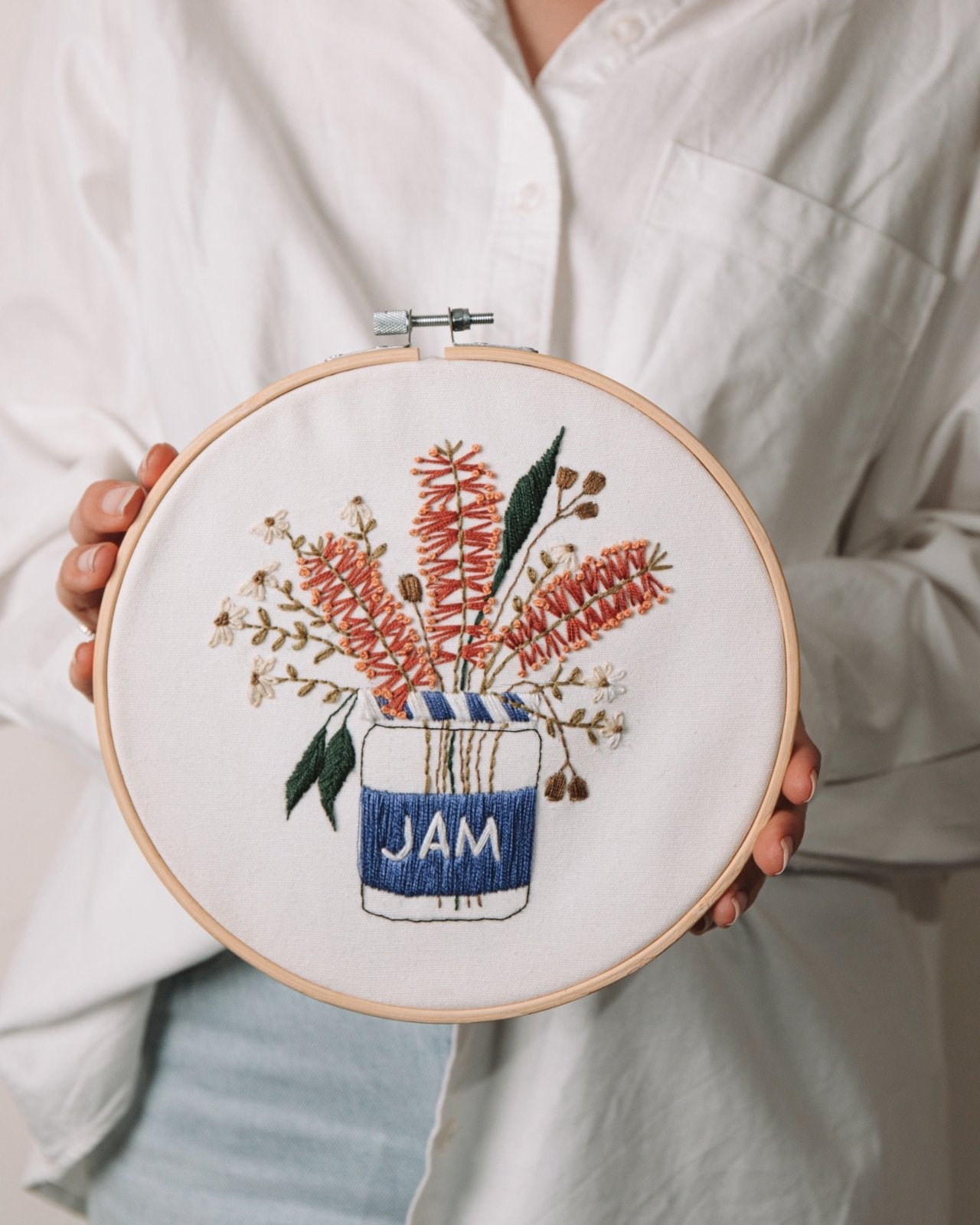 Girl in white shirt and blue jeans holding the completed Blue Jam embroidery kit