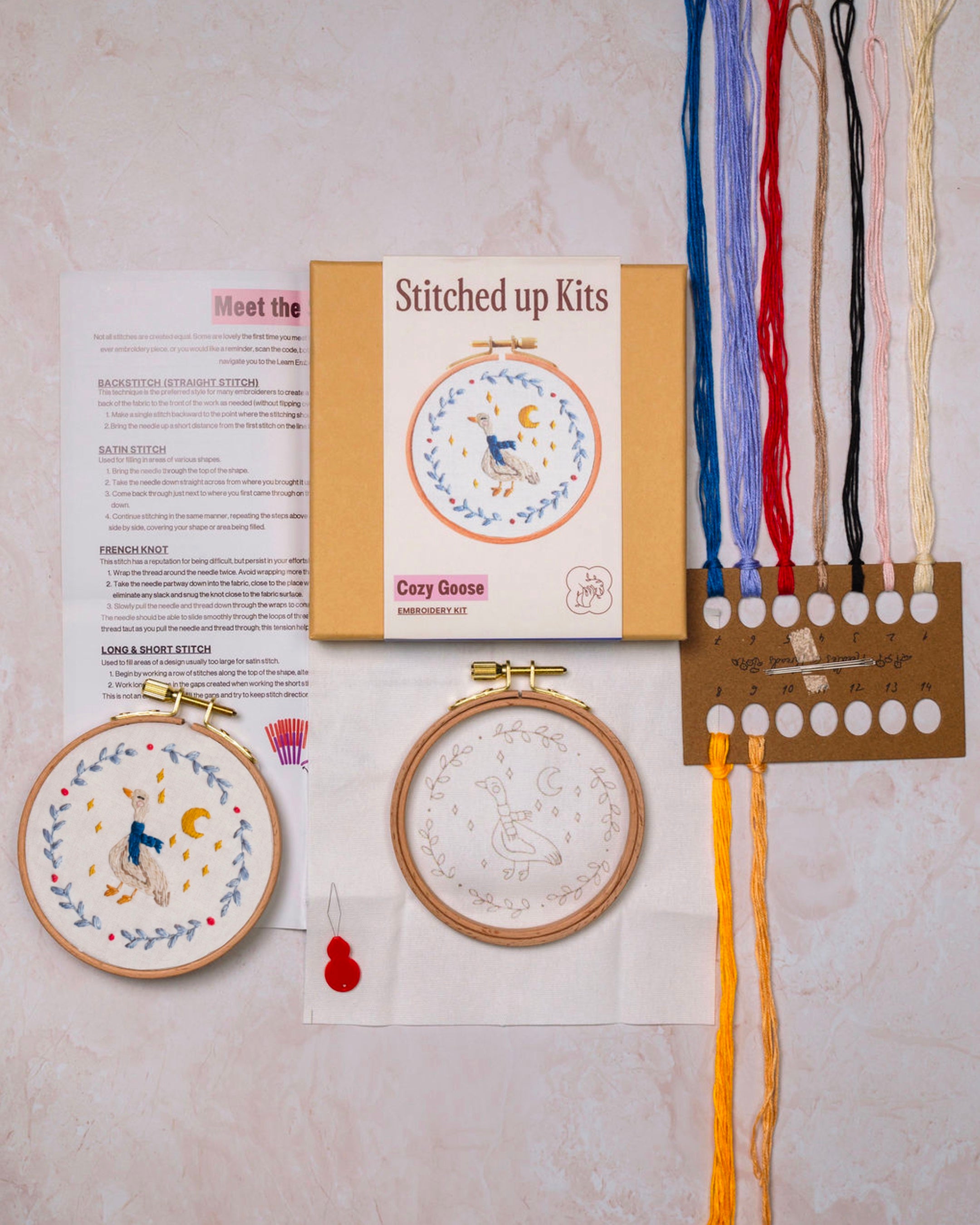 Embroidery kit with two completed pieces, a box labeled 'Stitched up Kits', and colorful threads on a light background.