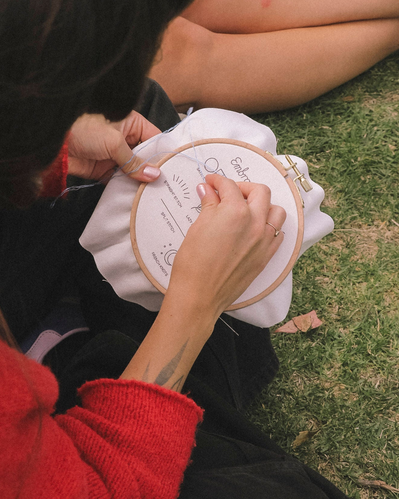 Person sitting on grass working on a embroidery hoop with a white cushion