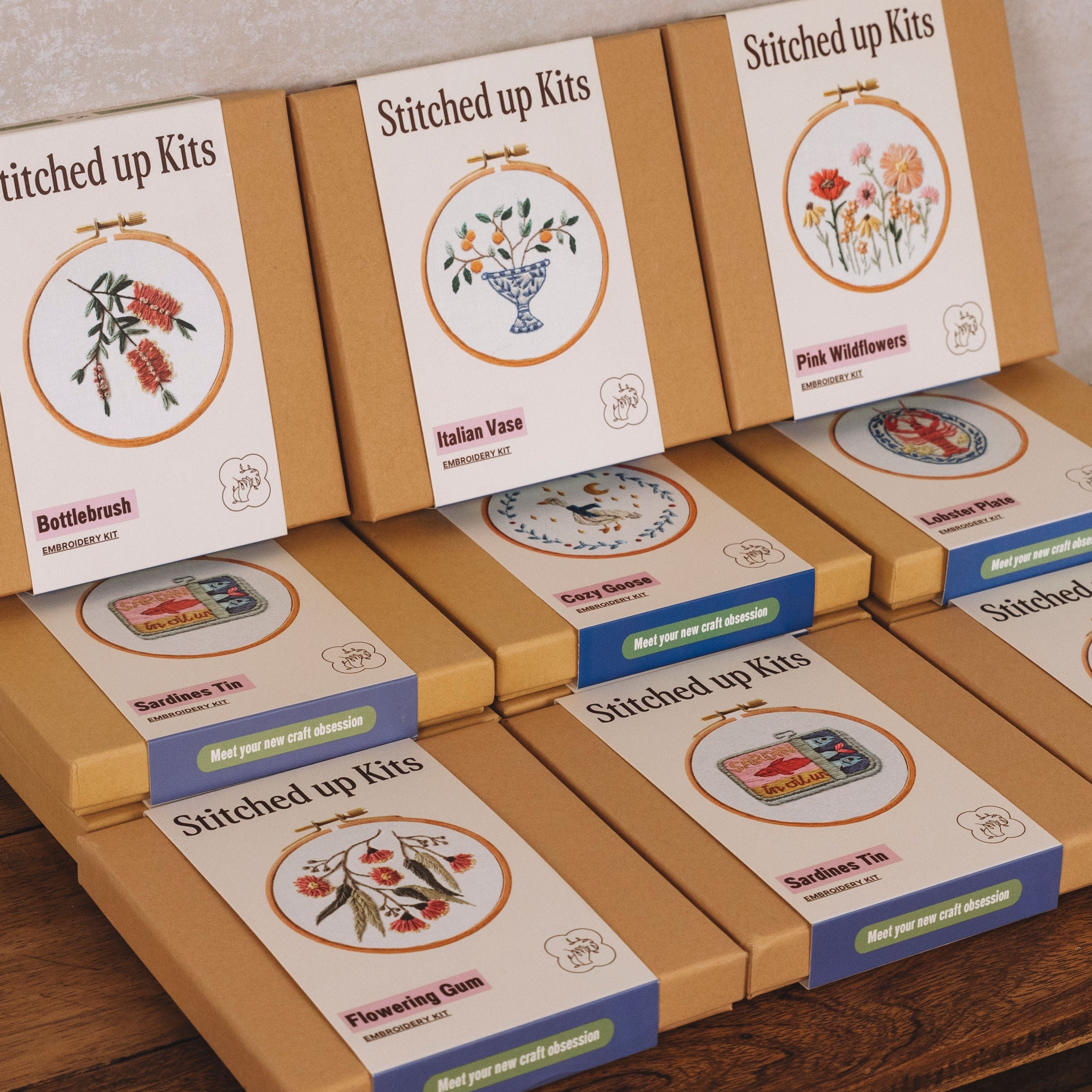 Rows of neatly arranged embroidery kits in simple brown boxes featuring floral and vintage tin designs on their covers